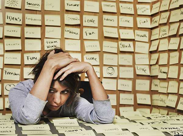 Woman at desk surrounded in adhesive notes, head in hands